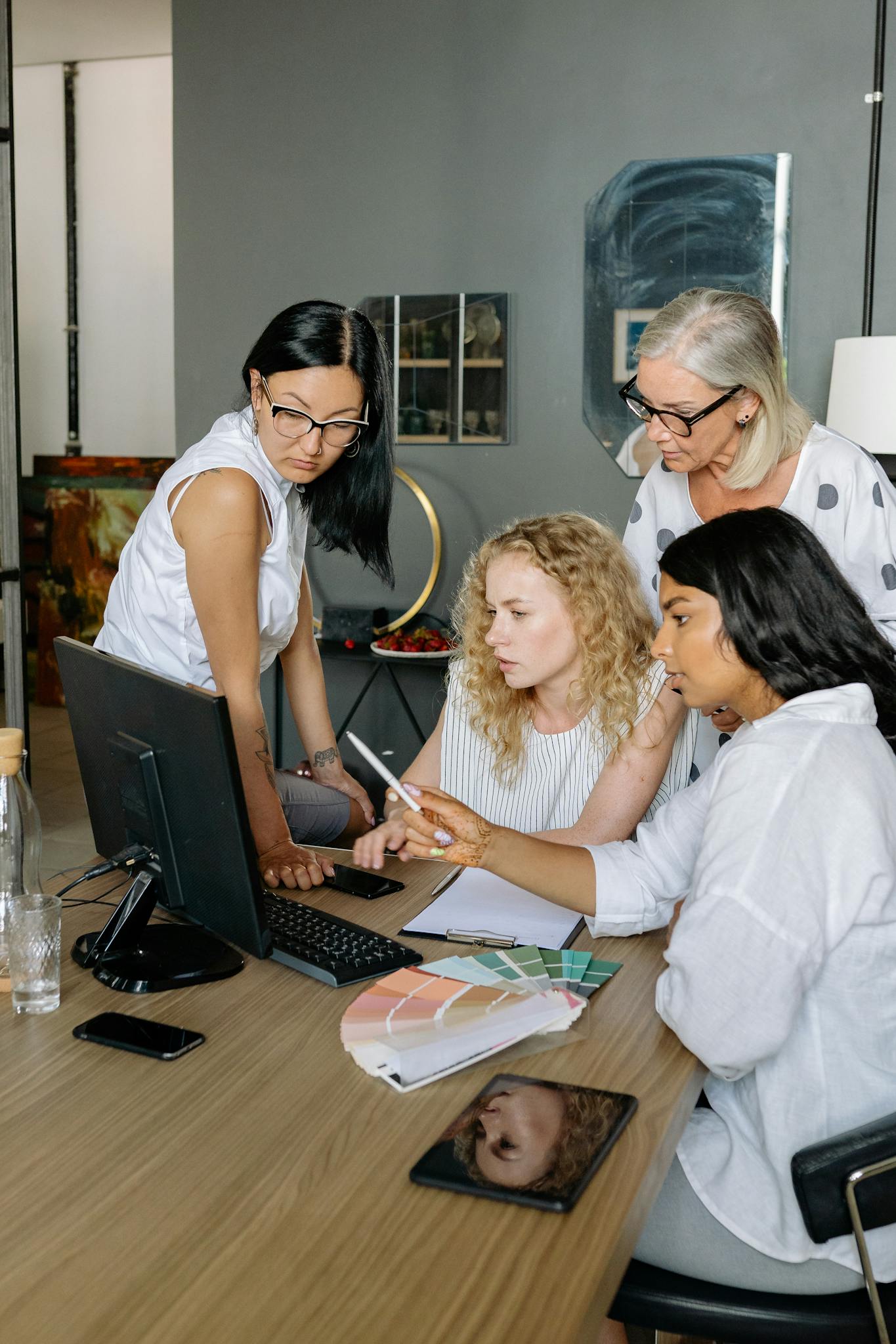 Four businesswomen collaborating over a computer in a modern office, showcasing teamwork and diversity.